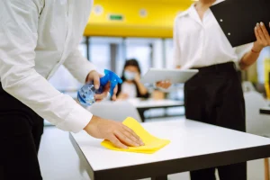Worker disinfecting a school desk with spray and cloth to maintain student health and hygiene