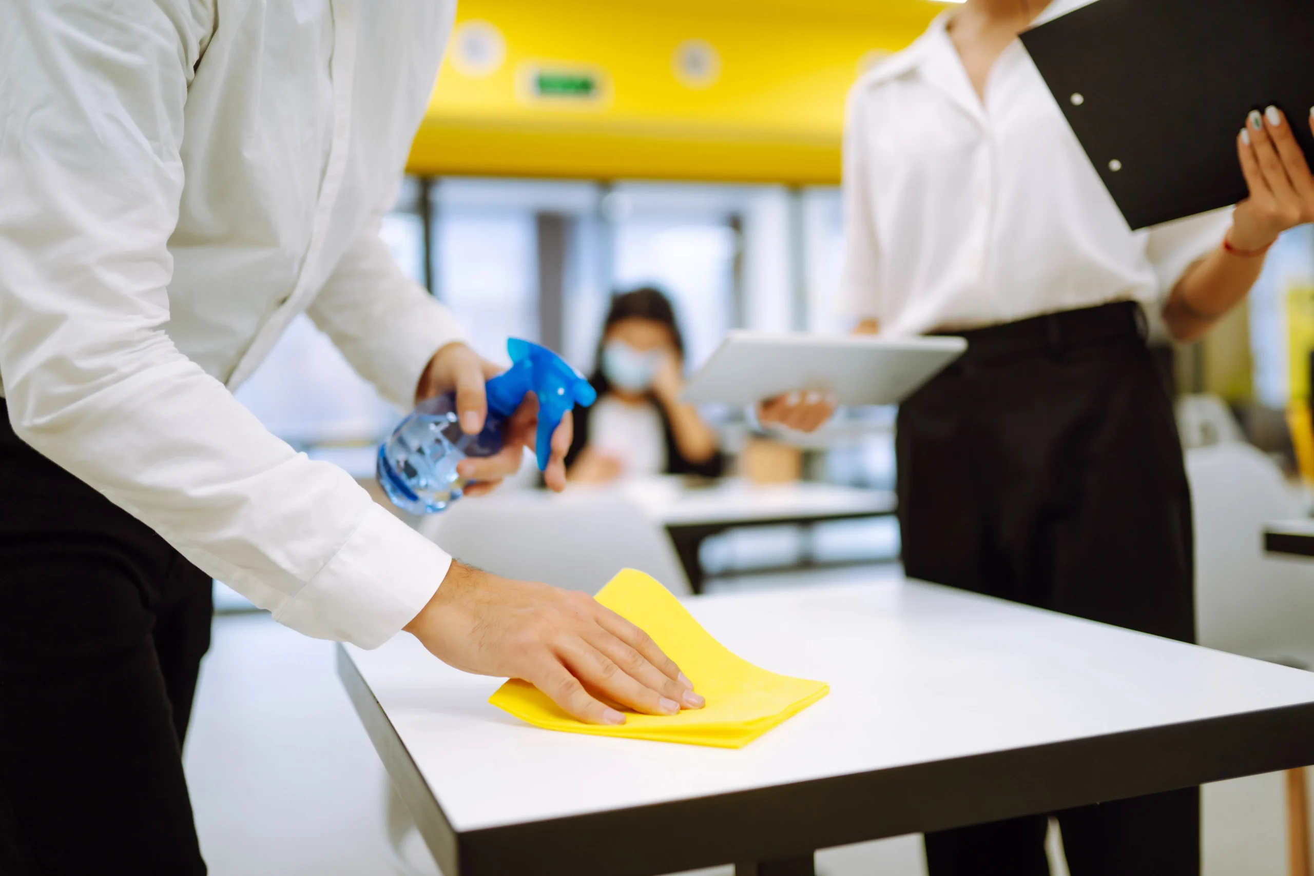 Worker disinfecting a school desk with spray and cloth to maintain student health and hygiene